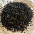 Close-up of loose Lapsang Souchong black tea leaves from Fujian province, dark and finely twisted on parchment paper.