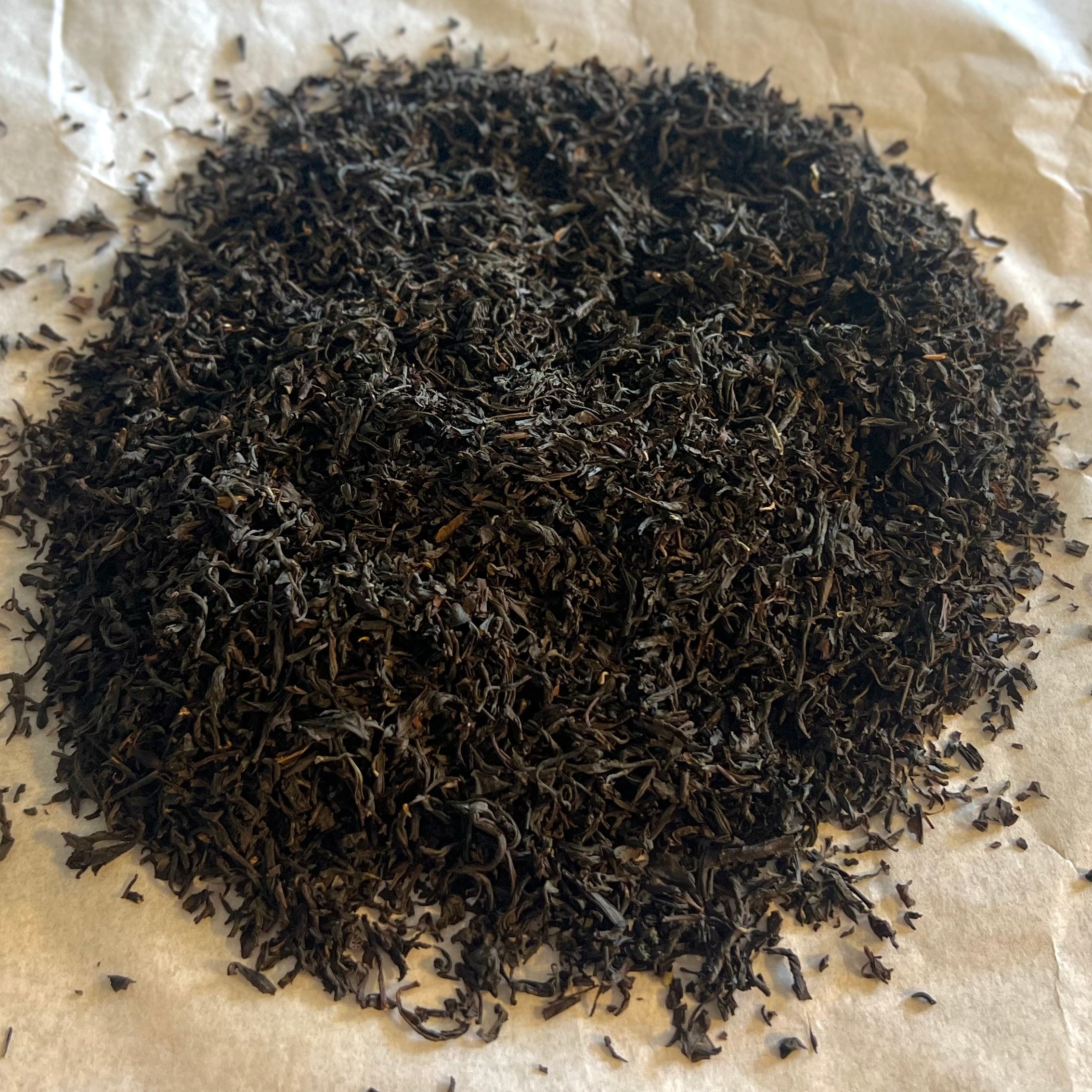 Close-up of loose Lapsang Souchong black tea leaves from Fujian province, dark and finely twisted on parchment paper.