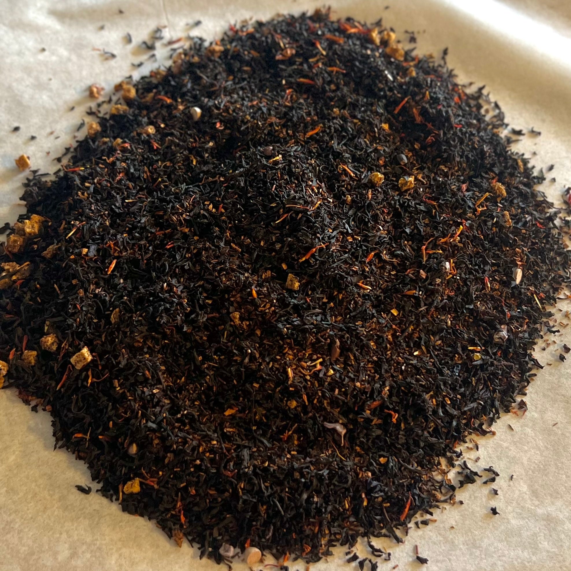 Close-up of Mango Affairs loose black and rooibos tea blend with dark mango pieces and chocolate hints on parchment paper
