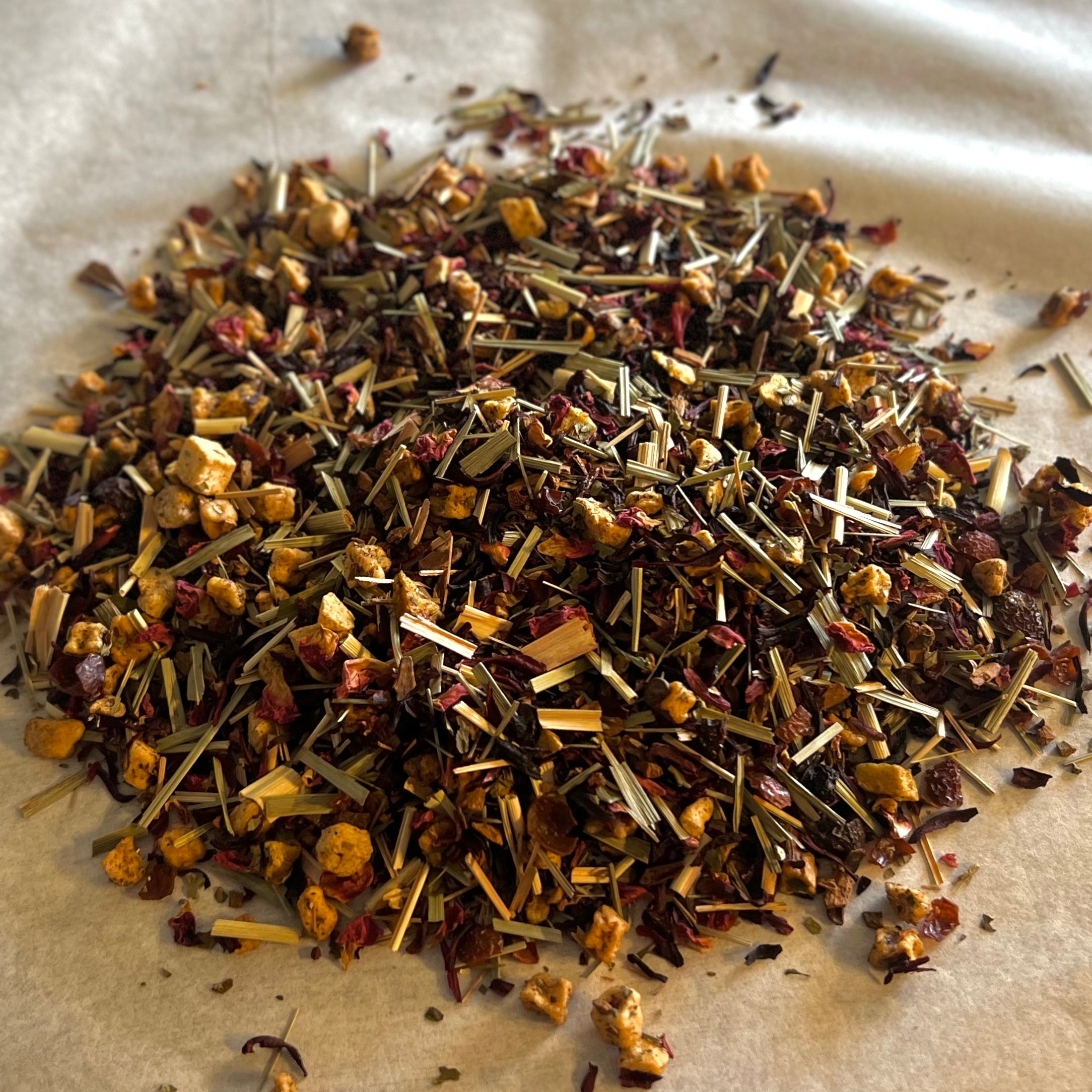 Close-up of Mango Tango caffeine-free tea blend with dried hibiscus, mango, peach pieces, cinnamon, and lemongrass on parchment paper