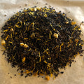 Close-up of Marigold Peach Oolong loose leaf tea blend with dark oolong leaves, marigold petals, and peach pieces on parchment paper