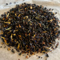 Close-up of Mariposa Oolong loose tea blend with rolled leaves, blue butterfly pea flowers, orange peel, and dried fruit pieces.