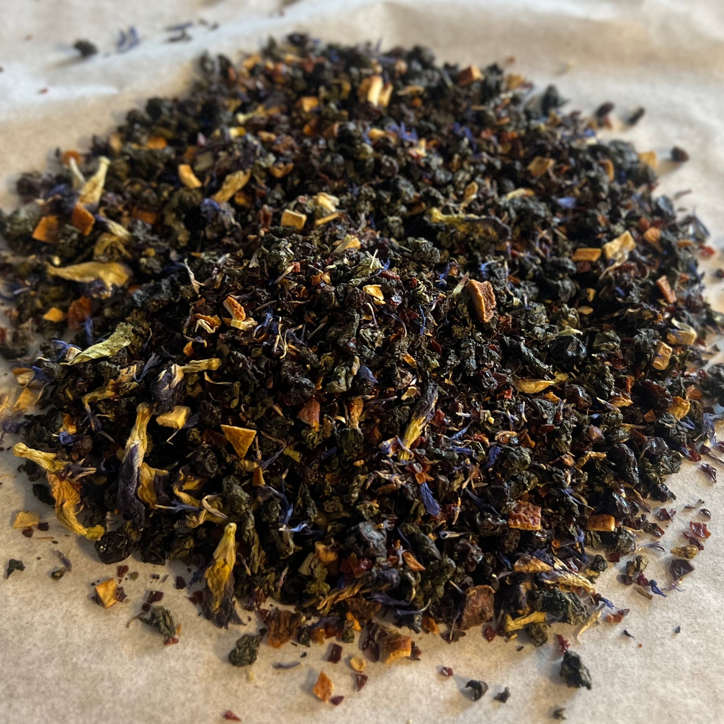 Close-up of Mariposa Oolong loose tea blend with rolled leaves, blue butterfly pea flowers, orange peel, and dried fruit pieces.
