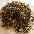 Close-up of Misty Mountain Mornings tea blend with dark gunpowder green leaves and bright yellow flower petals on white background