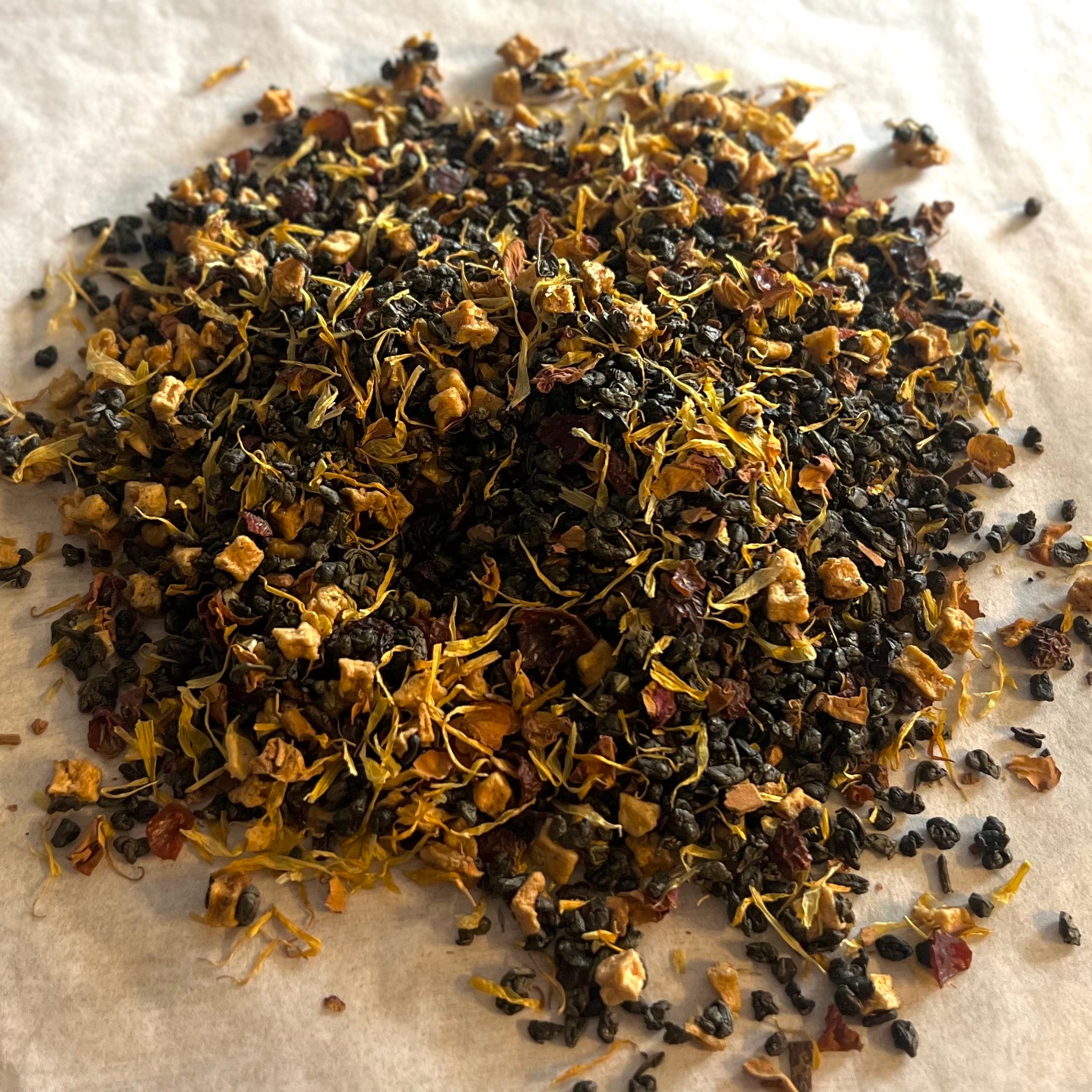 Close-up of Misty Mountain Mornings tea blend with dark gunpowder green leaves and bright yellow flower petals on white background