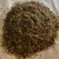 Close-up of Momma’s Tea Nourish blend with rooibos, raspberry leaf, fennel seed, and spearmint on parchment paper background