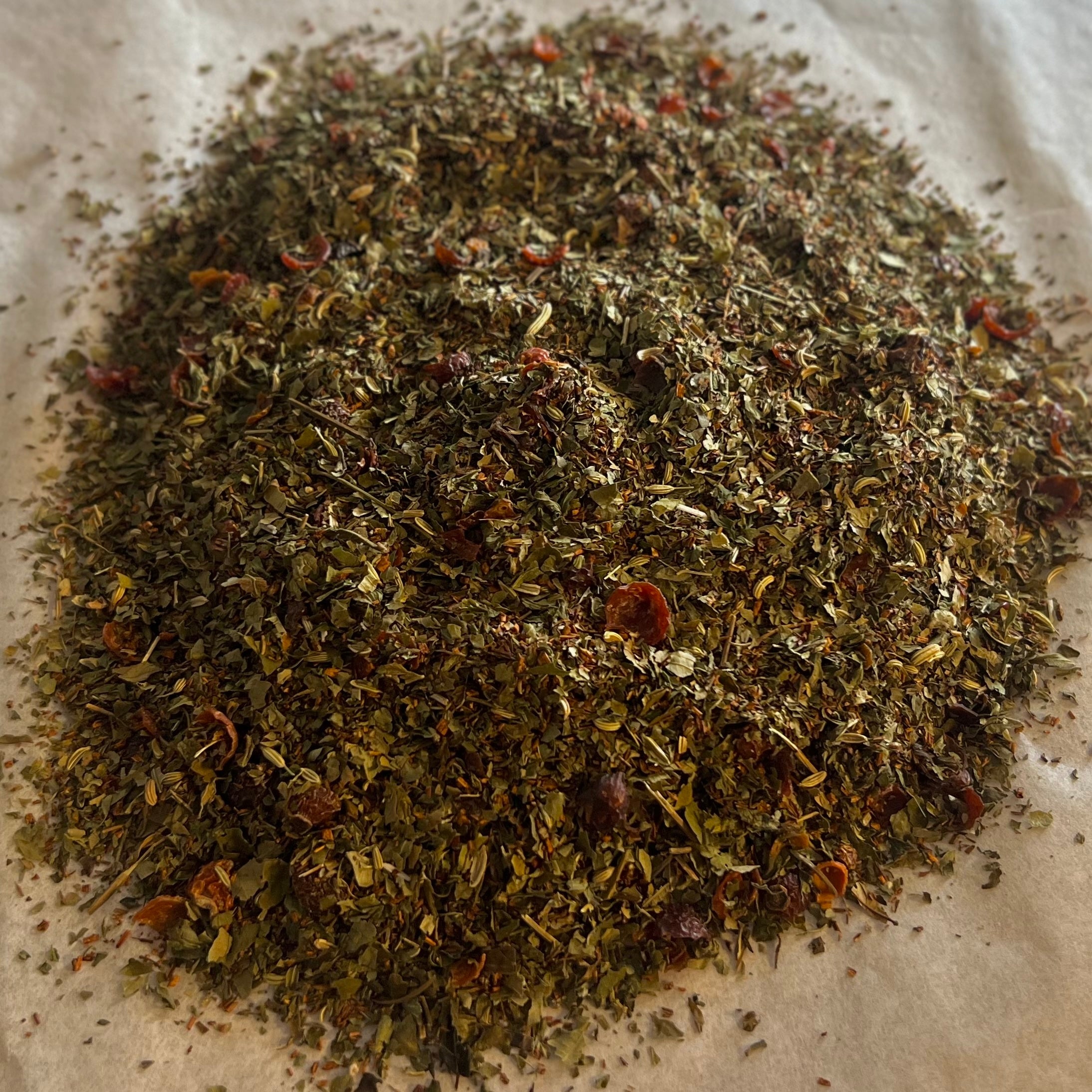 Close-up of Momma’s Tea Nourish blend with rooibos, raspberry leaf, fennel seed, and spearmint on parchment paper background