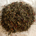 Close-up of Momma's Tea Settle herbal blend with chamomile, lemon balm, spearmint, ginger, and dried flower petals on parchment.