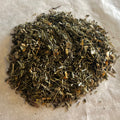 Close-up of loose Mood De-Stress herbal tea blend with green leaves and dried herbs on a light surface