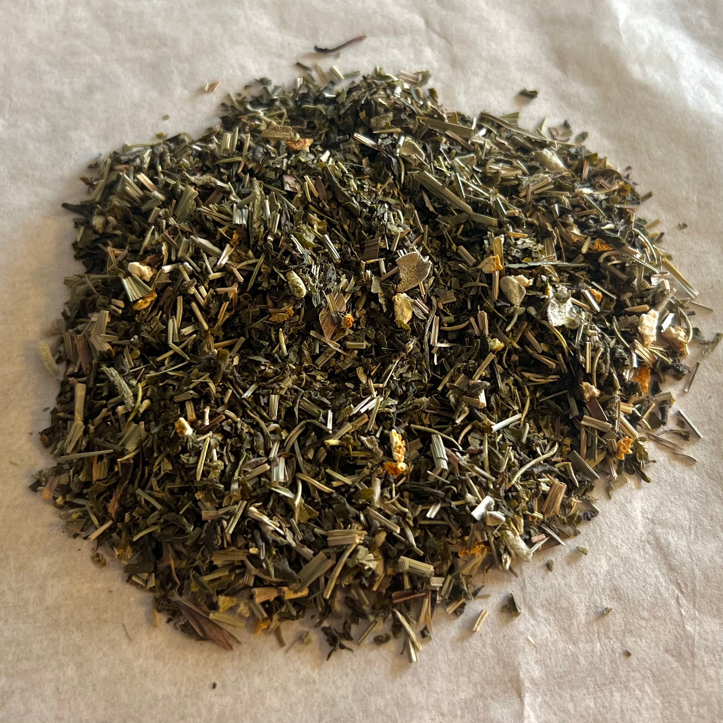 Close-up of loose Mood De-Stress herbal tea blend with green leaves and dried herbs on a light surface
