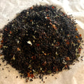 Close-up of Mountain Berry loose black tea blend with rosehip pieces and raspberry bits on light parchment paper.