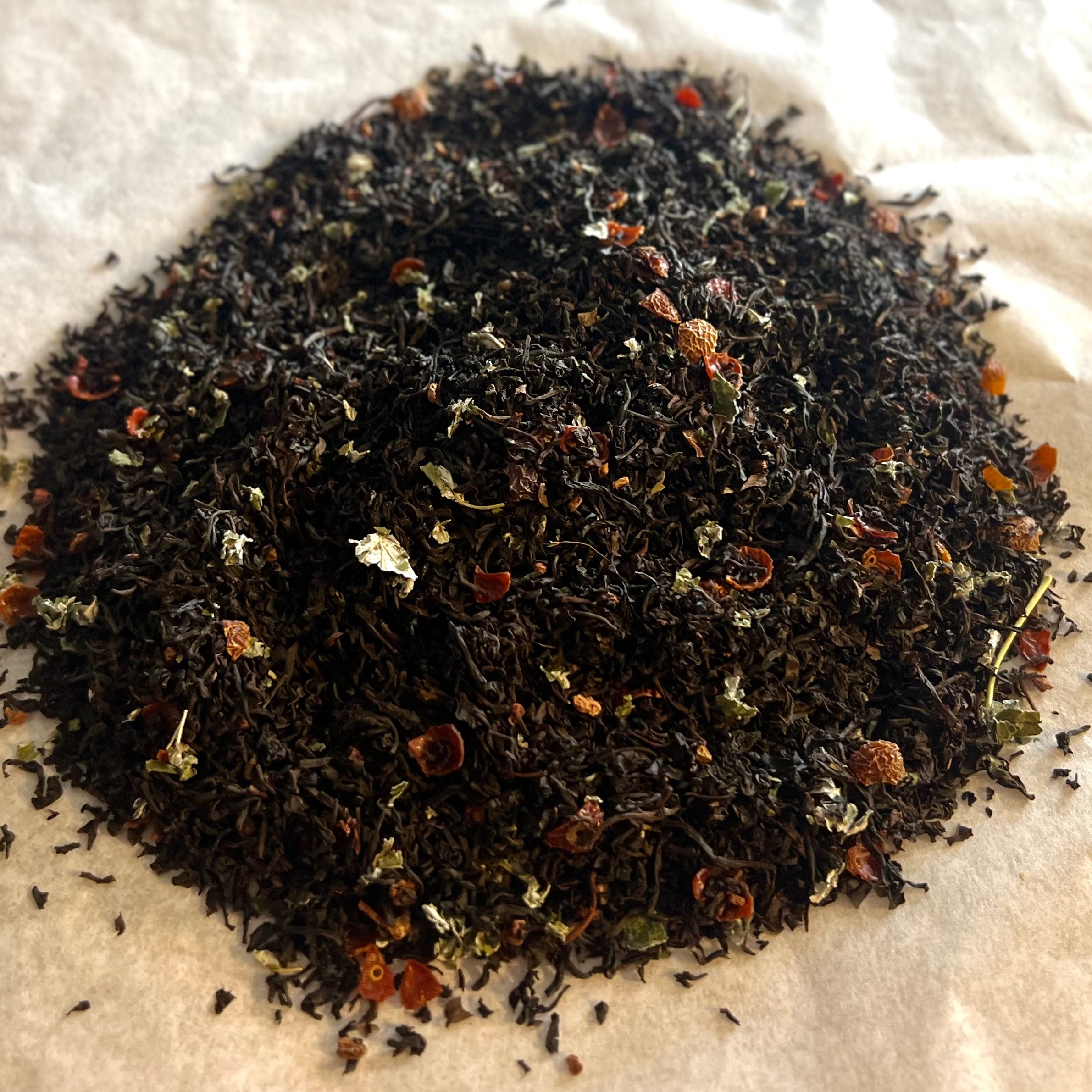 Close-up of Mountain Berry loose black tea blend with rosehip pieces and raspberry bits on light parchment paper.