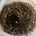 Close-up of Chai No. 26 loose black tea blend with cinnamon, spices, and coconut pieces on parchment paper