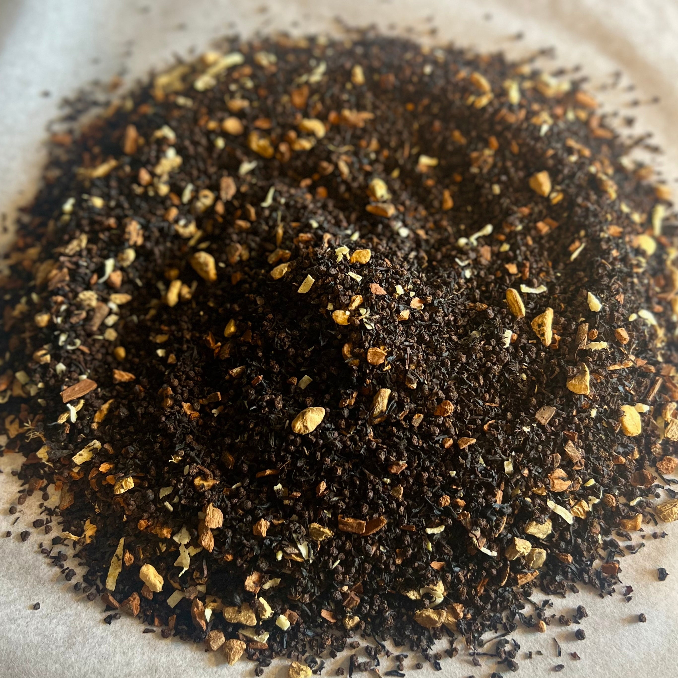 Close-up of Chai No. 26 loose black tea blend with cinnamon, spices, and coconut pieces on parchment paper