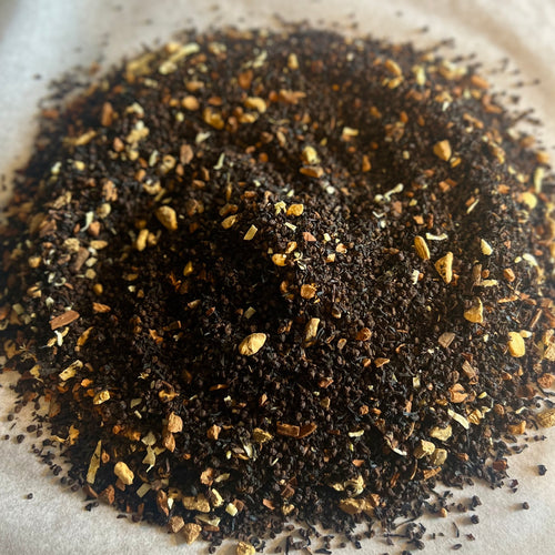 Close-up of Chai No. 26 loose black tea blend with cinnamon, spices, and coconut pieces on parchment paper