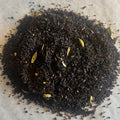 Close-up of loose black chai tea leaves blended with pale cardamom pods on a light textured surface.