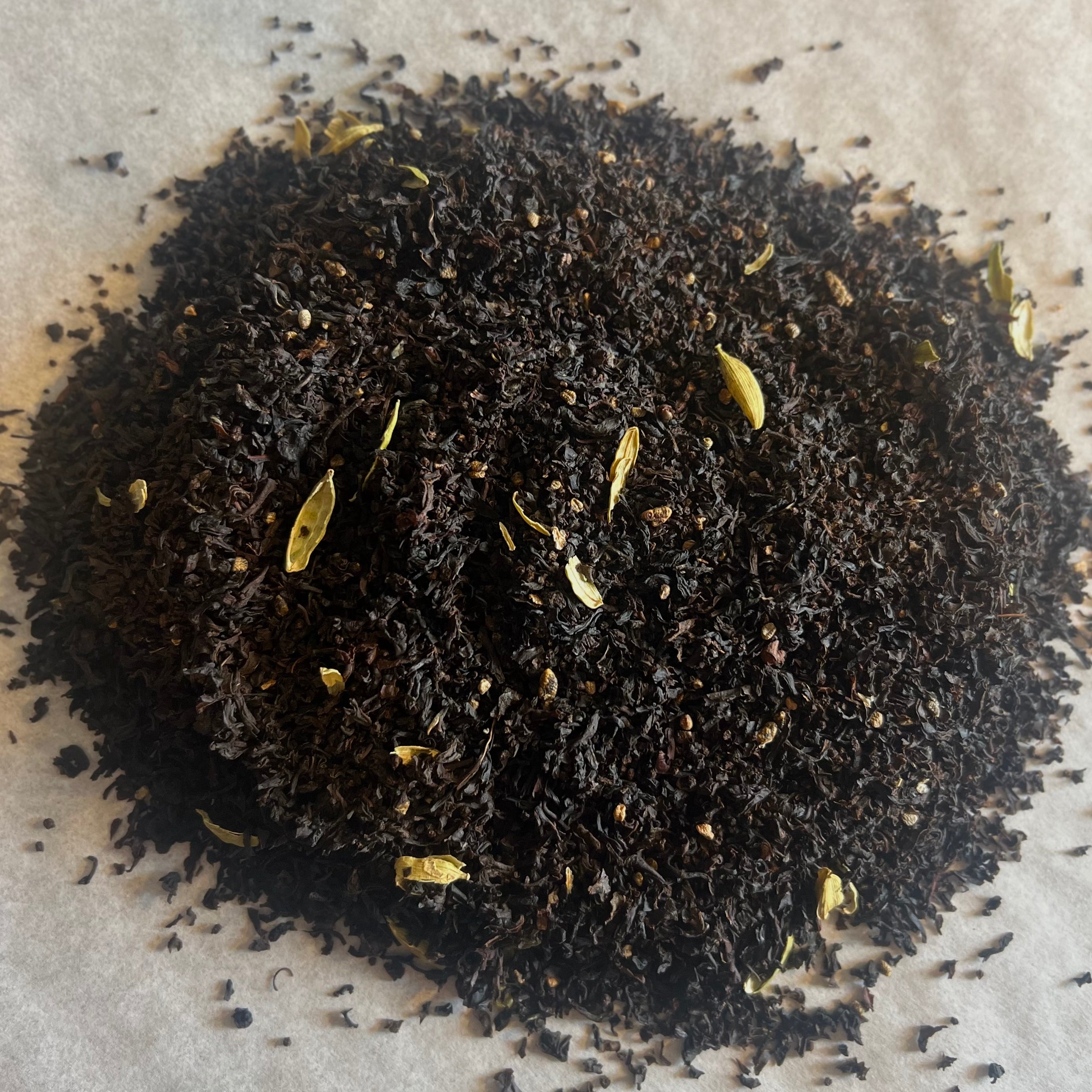 Close-up of loose black chai tea leaves blended with pale cardamom pods on a light textured surface.
