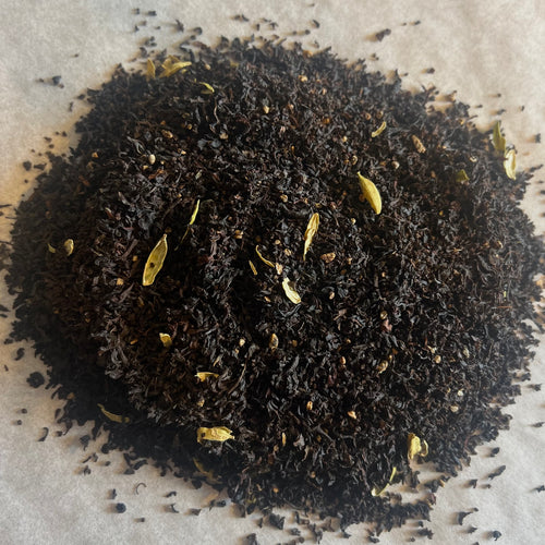 Close-up of loose black chai tea leaves blended with pale cardamom pods on a light textured surface.