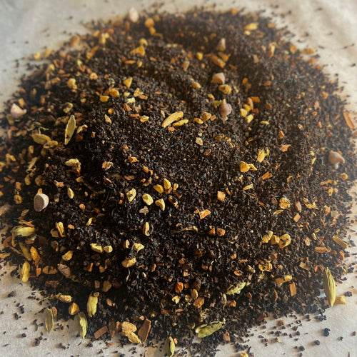 Close-up of Chai No. 62 loose black tea blend with ginger, cardamom, and chocolate chips on parchment paper.