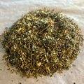 Close-up of Bright & Clear loose herbal tea blend with dried green leaves and yellow herbal pieces on parchment paper