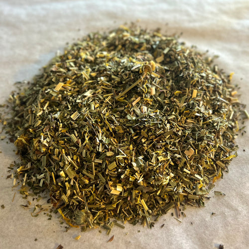 Close-up of Bright & Clear loose herbal tea blend with dried green leaves and yellow herbal pieces on parchment paper