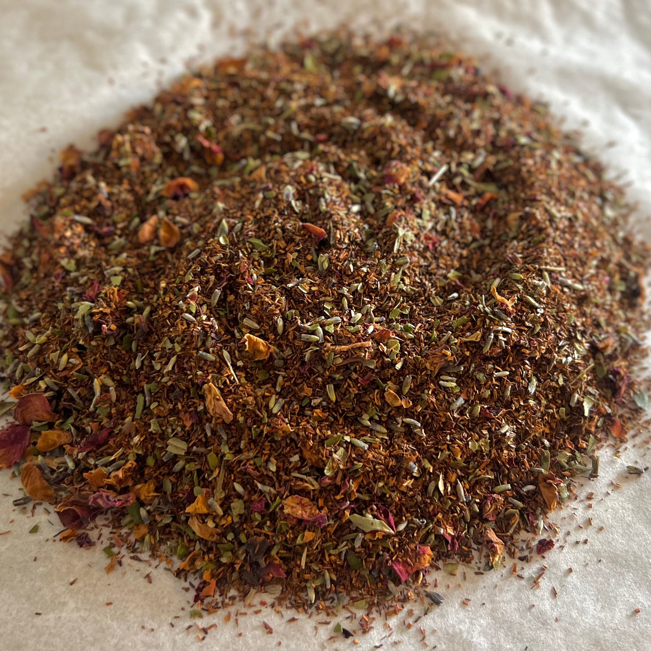 Close-up of Earl Grey Sampler loose tea blend with rooibos, herbs, flower petals, and bergamot citrus pieces on parchment paper.