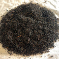 Close-up of loose Foggy Courtyard Earl Grey black tea leaves with dark twisted leaves on a light surface