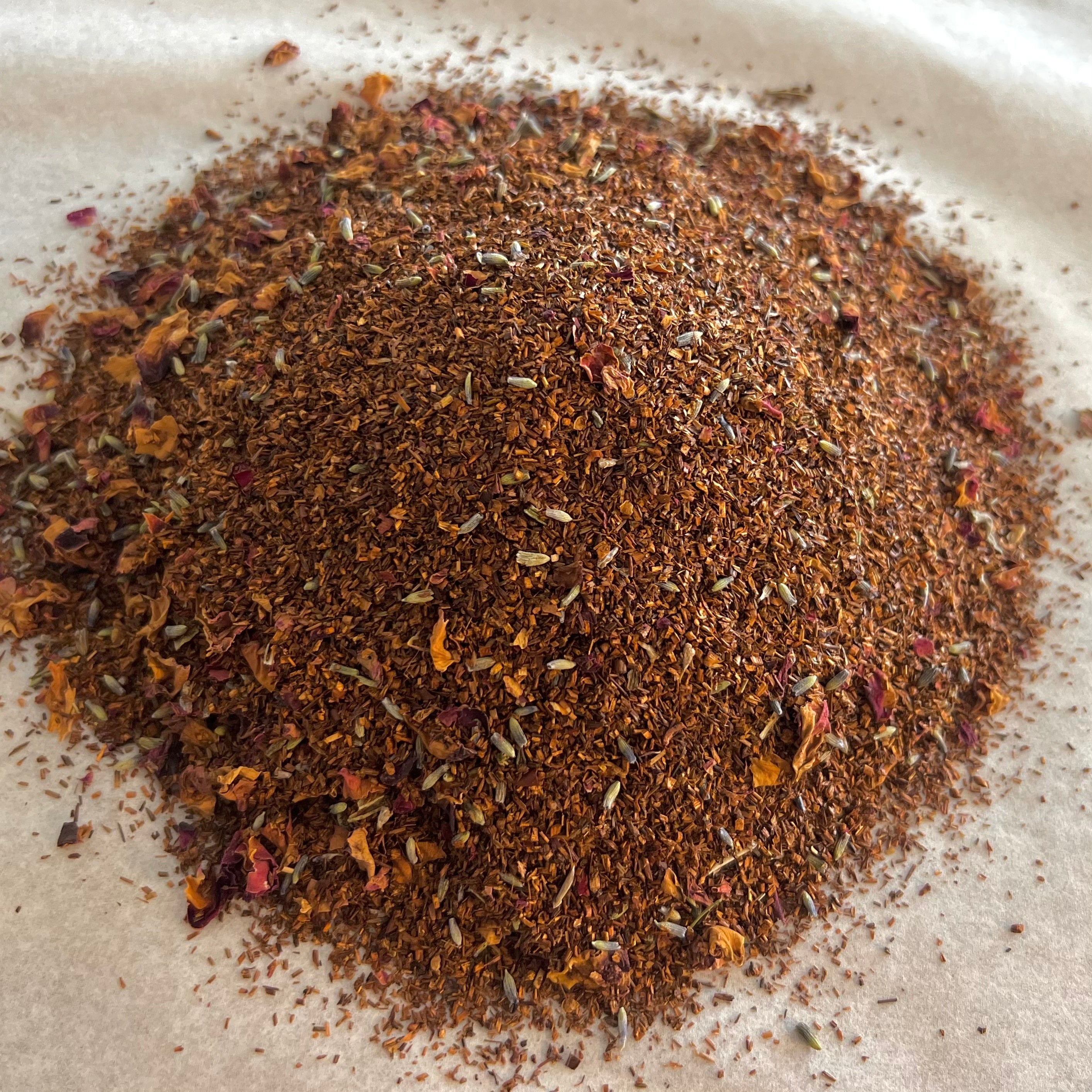 Close-up of French Lavender rooibos tea blend with fine reddish leaves and scattered lavender and flower petals on light surface