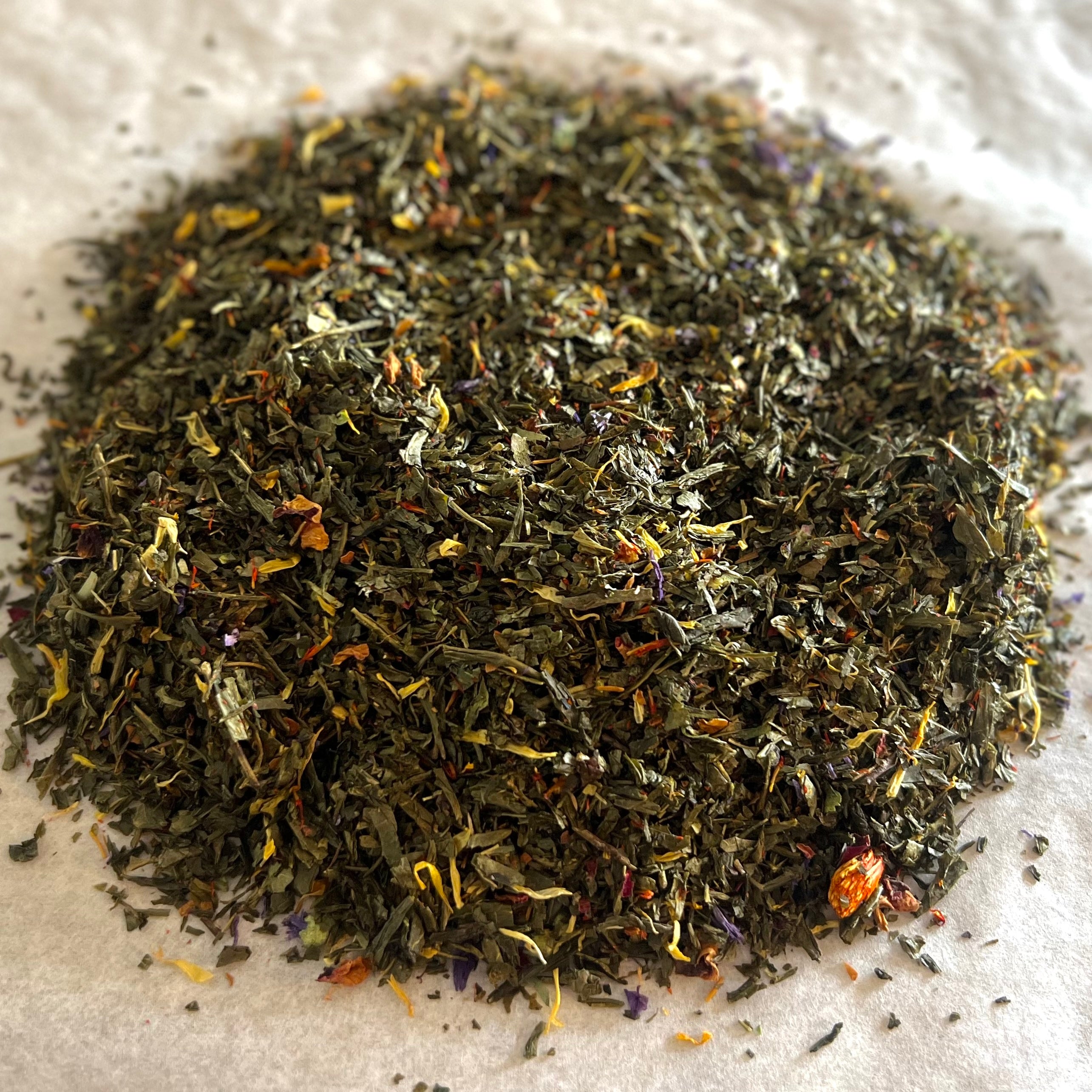 Close-up of Gentle Bloom loose green tea blend with rose petals, marigold, safflower, and mallow blossoms on white paper.