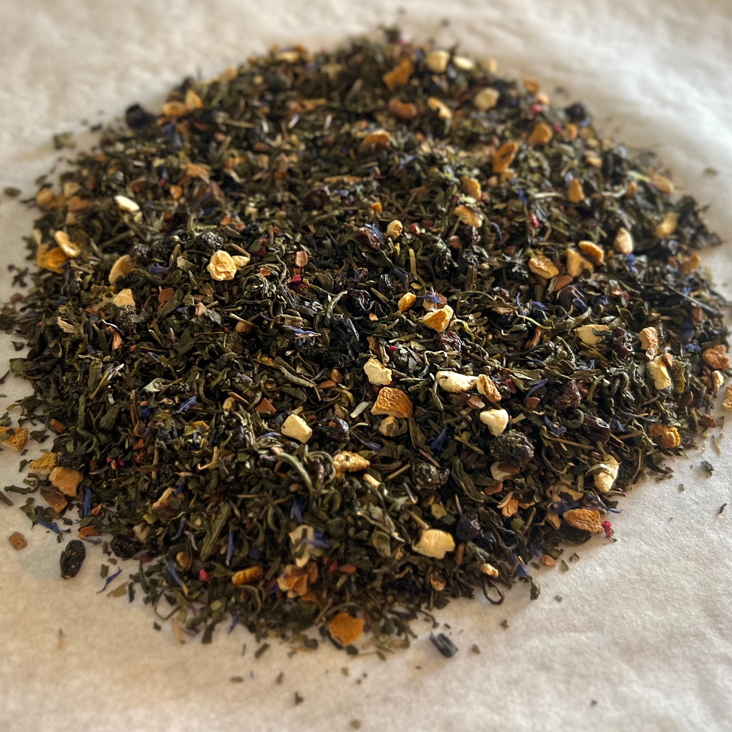 Close-up of Get Figgy w/It loose green tea blend with fig pieces, cinnamon, orange zest, and delicate floral hints on white surface