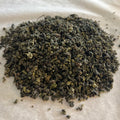 Close-up of tightly rolled Golden Flower Oolong tea leaves with dark green and golden hues on parchment paper.