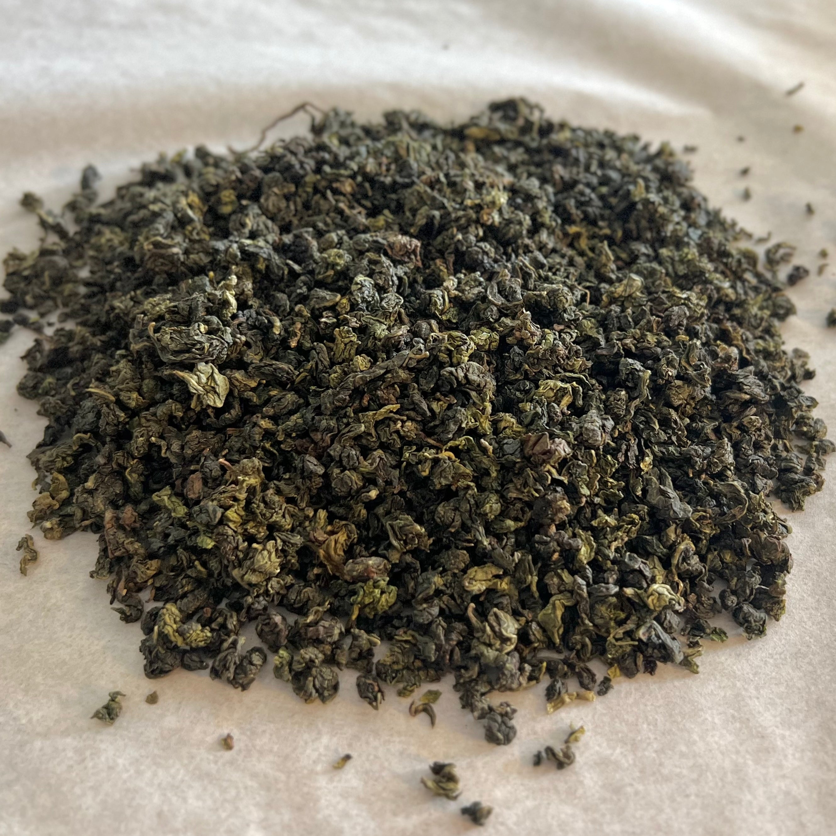 Close-up of tightly rolled Golden Flower Oolong tea leaves with dark green and golden hues on parchment paper.