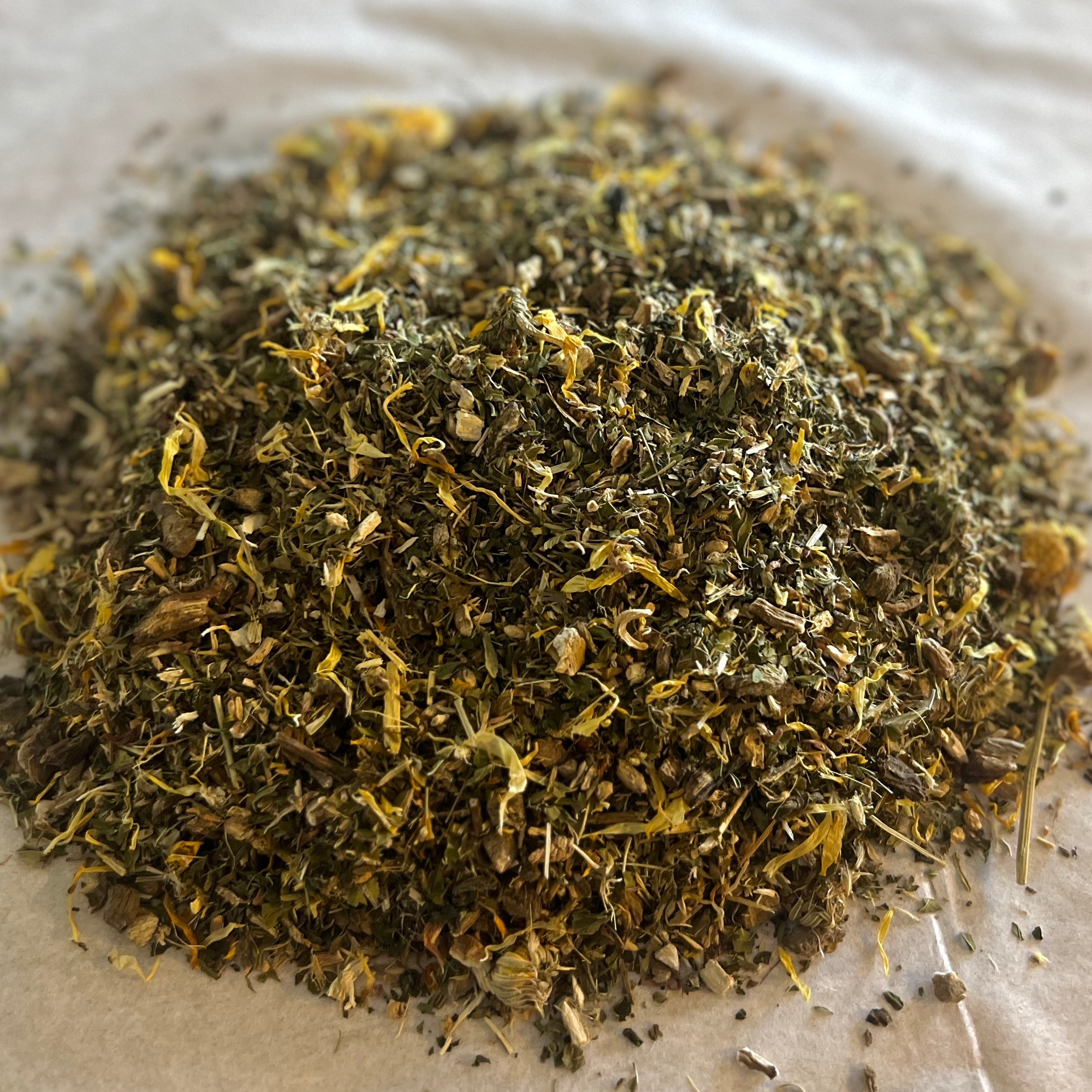 Close-up of Holding Center herbal tea blend with dried burdock, dandelion, and marigold petals on light background.