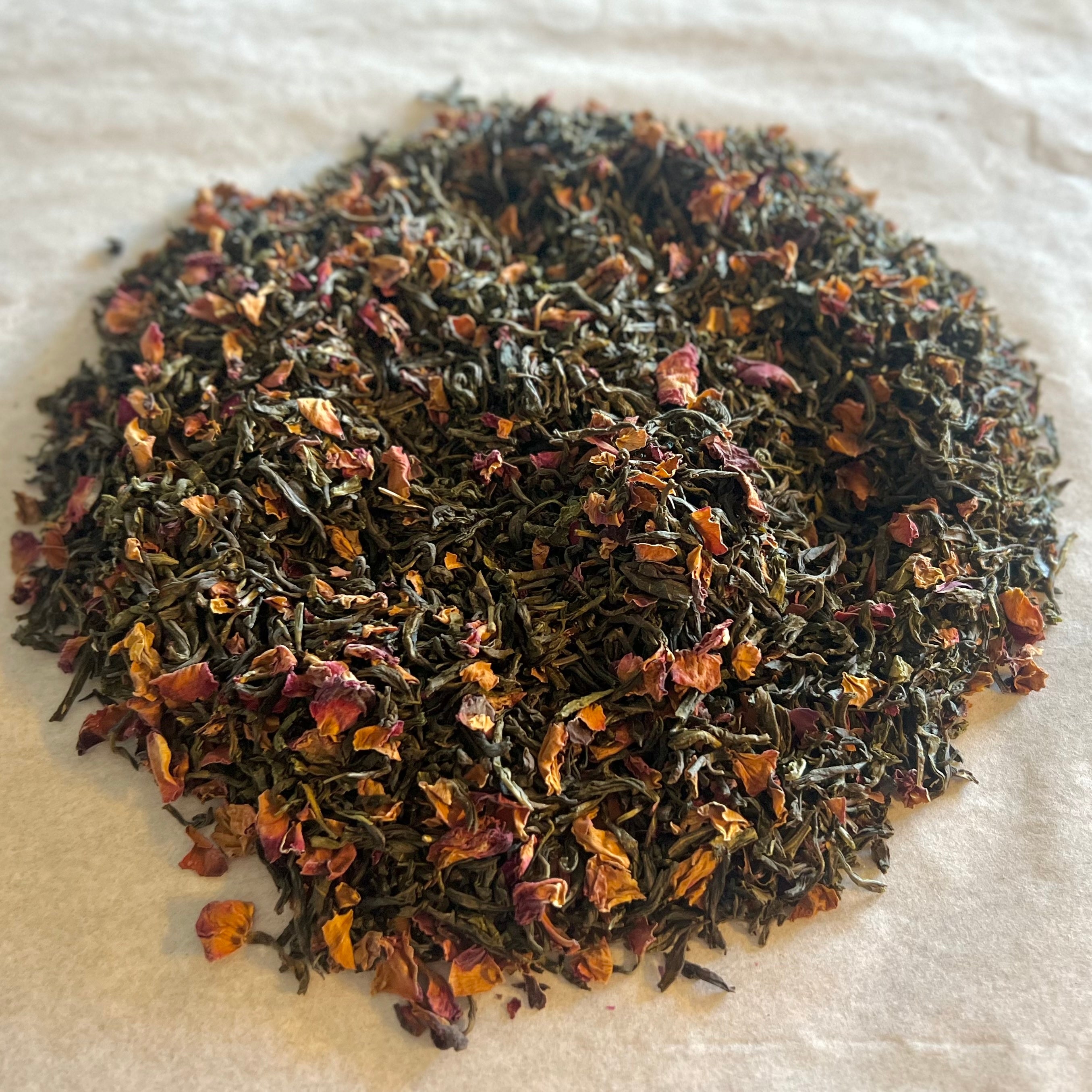 Loose Jasmine Oolong tea leaves mingled with delicate dried jasmine petals on a white surface, ready for brewing.