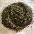 Close-up of loose Mint Condition green tea blend with spearmint leaves and small raspberry and watermelon pieces on white surface