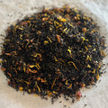 Close-up of Nutty Honey Crunch loose black tea blend with toasted nuts, golden petals, and small spice pieces on parchment paper