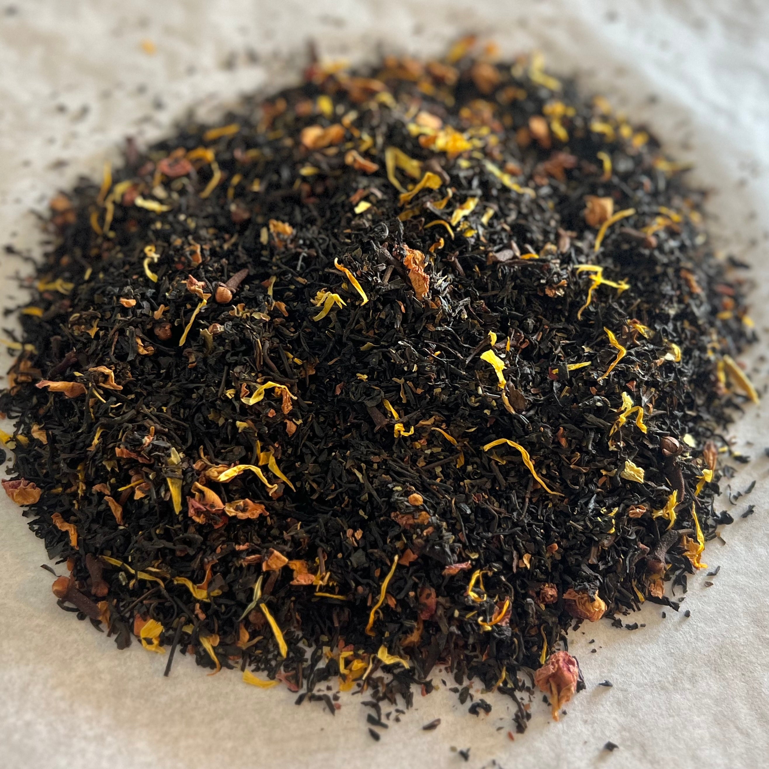 Close-up of Nutty Honey Crunch loose black tea blend with toasted nuts, golden petals, and small spice pieces on parchment paper