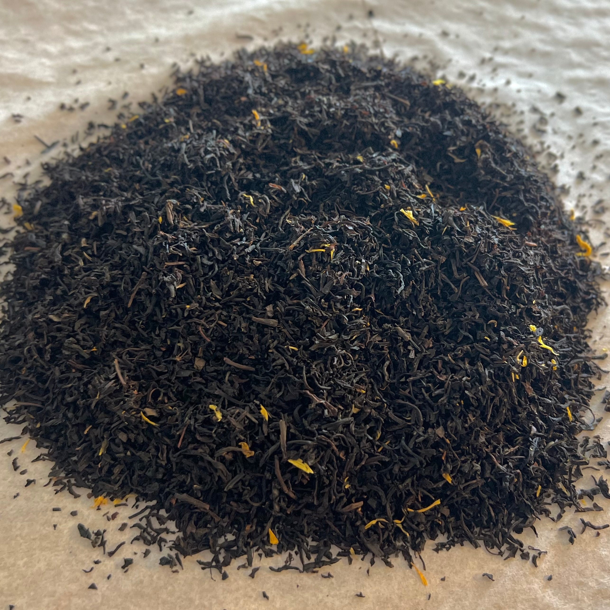 Loose Peach Bellini black tea blend with dark leaves and subtle yellow flower petals on a light textured surface