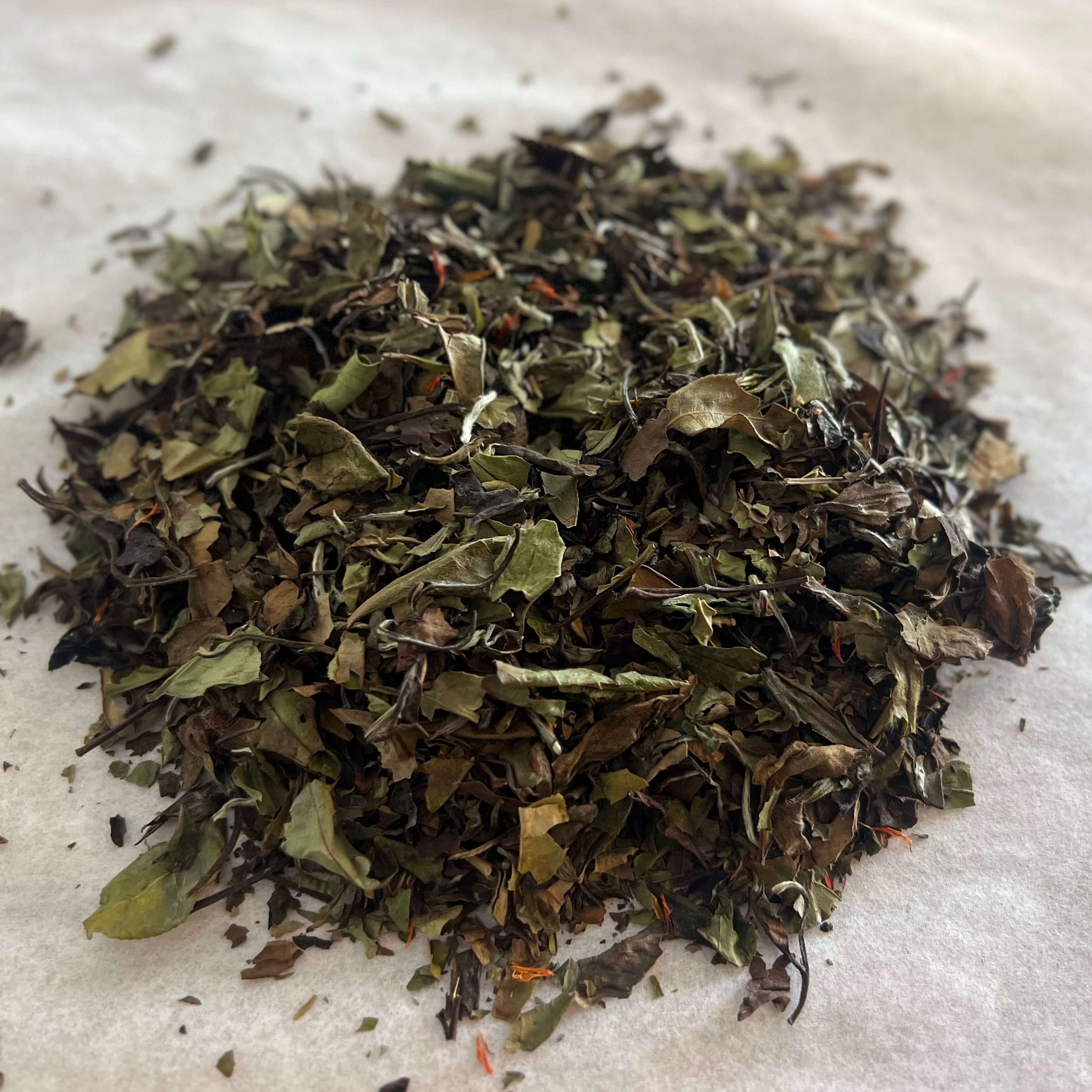 Close-up of loose Pomegranate & Peony white tea blend with dried leaves, pomegranate peel, and safflower petals on light background