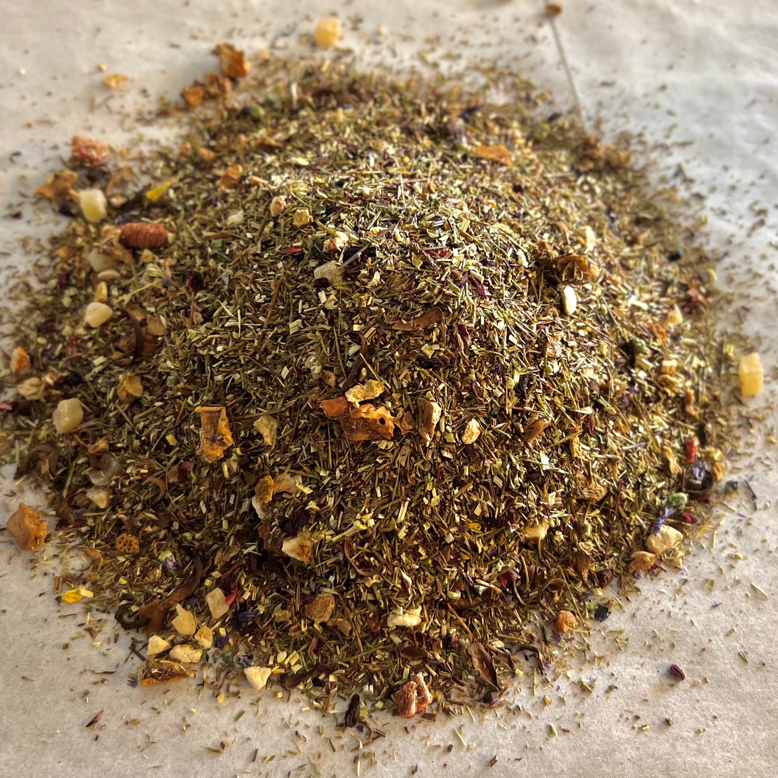 Close-up of Ruby-Red Dragon rooibos tea blend with dragonfruit, mango, apple pieces, and citrus peel on parchment paper