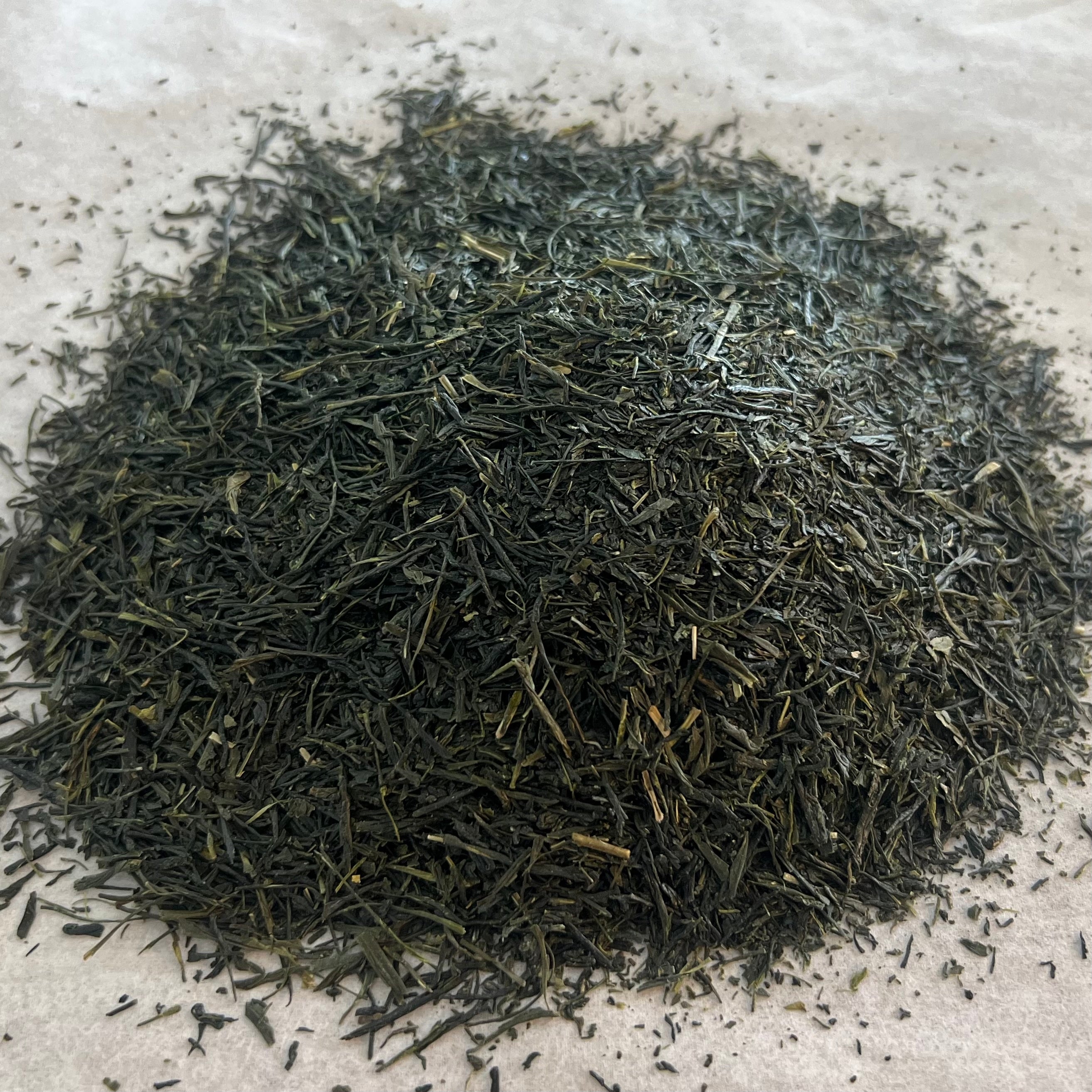 Loose Sencha Arihara Japanese green tea leaves, finely cut with a deep green hue on a light surface.