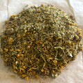 Close-up of Settle & Soothe herbal tea blend with chamomile, calendula petals, and dried herbs on parchment paper.
