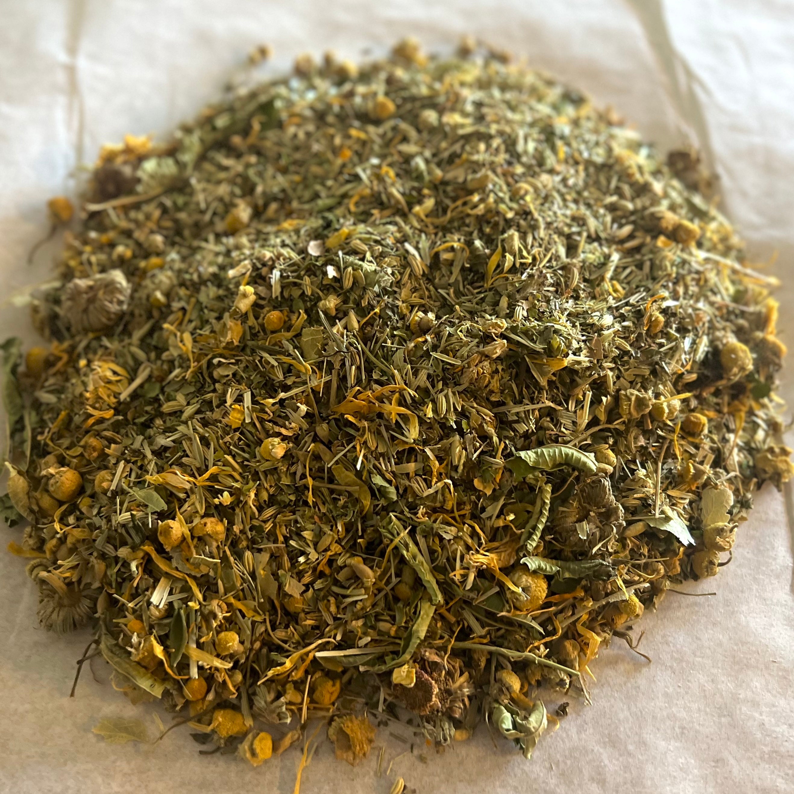 Close-up of Settle & Soothe herbal tea blend with chamomile, calendula petals, and dried herbs on parchment paper.