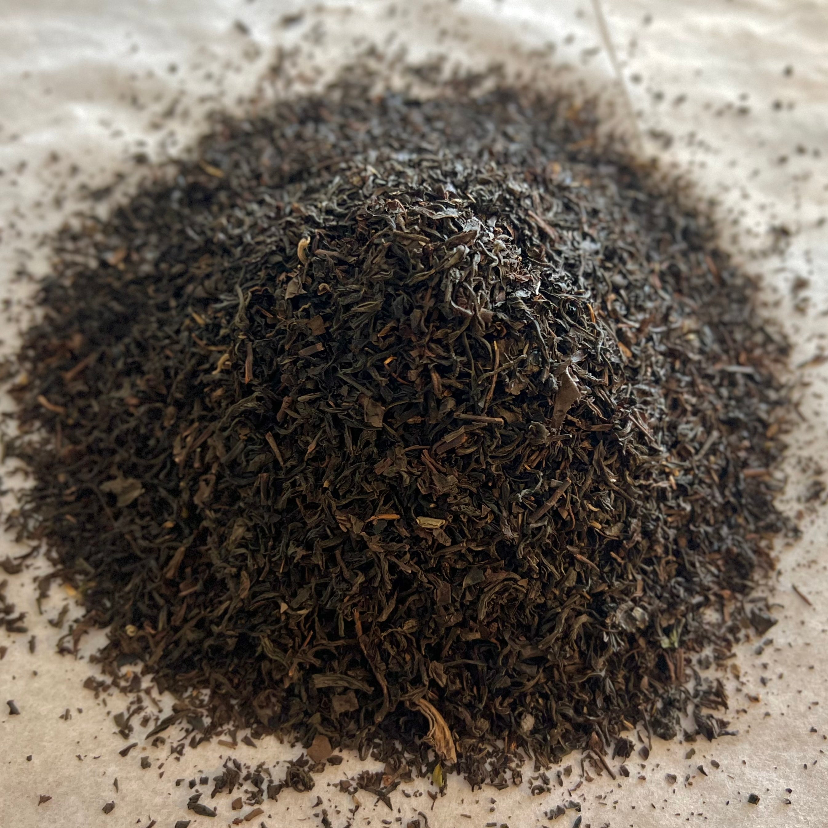Close-up of loose Smokey Vibes tea blend with dark, finely textured pine-smoked Lapsang Souchong leaves on parchment paper