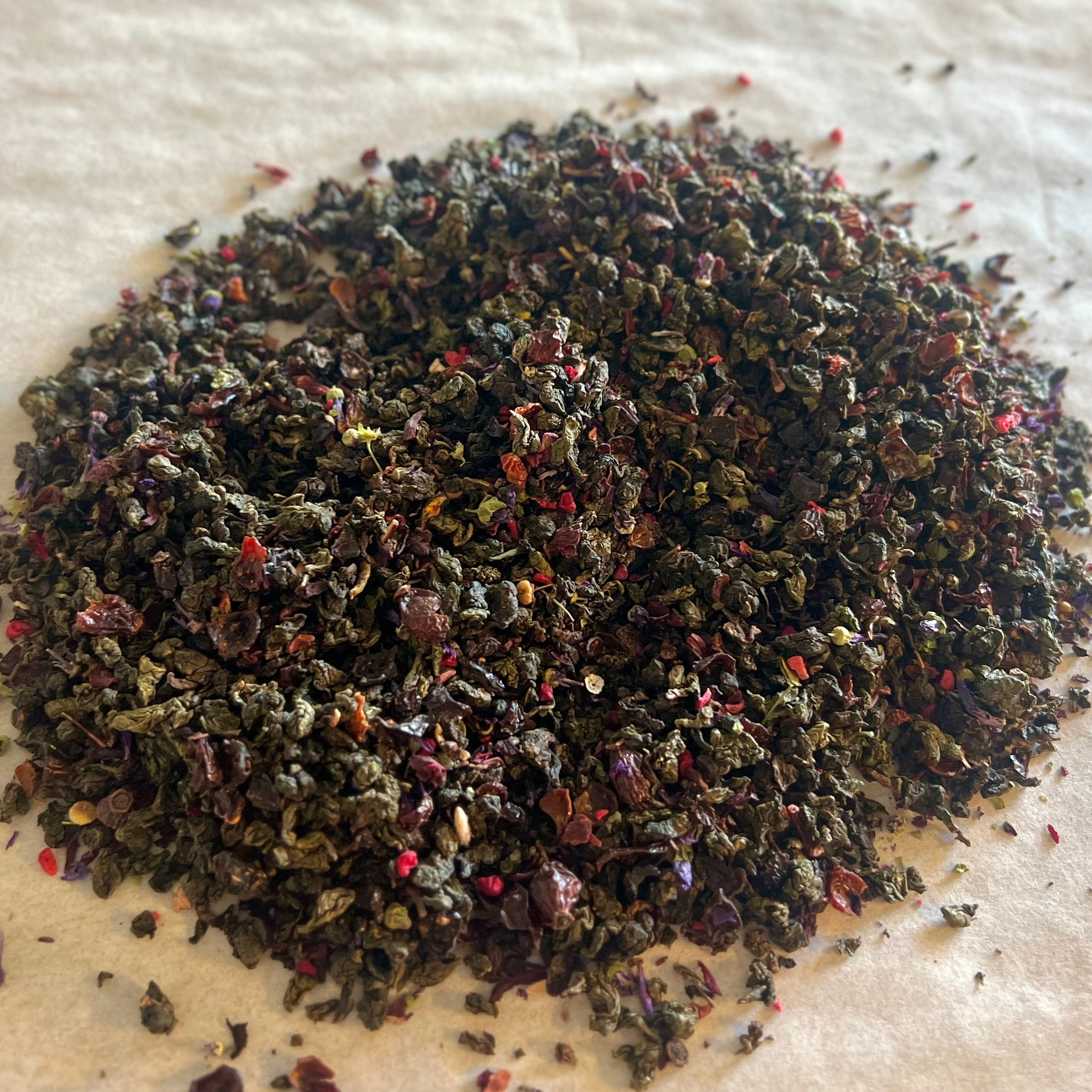 Close-up of Sun-Kissed Oolong loose tea blend with dark rolled oolong leaves and bright red floral petals on light surface