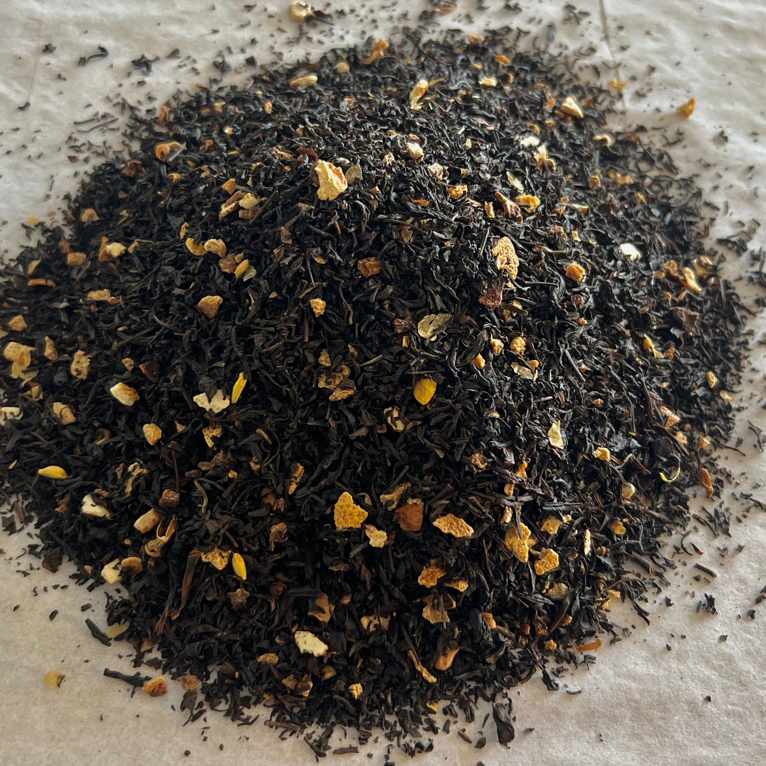 Close-up of The Grey Lady loose black tea blend with dark leaves, bergamot, and bright orange peel pieces on parchment paper