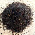 Close-up of Whiskey & Wit black tea blend with dark leaves and hints of spices on a light surface ready for brewing