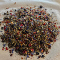 Close-up of Whispering Petals loose tea blend with rose petals, rose hips, cherry, blueberry, raspberry pieces on a light surface