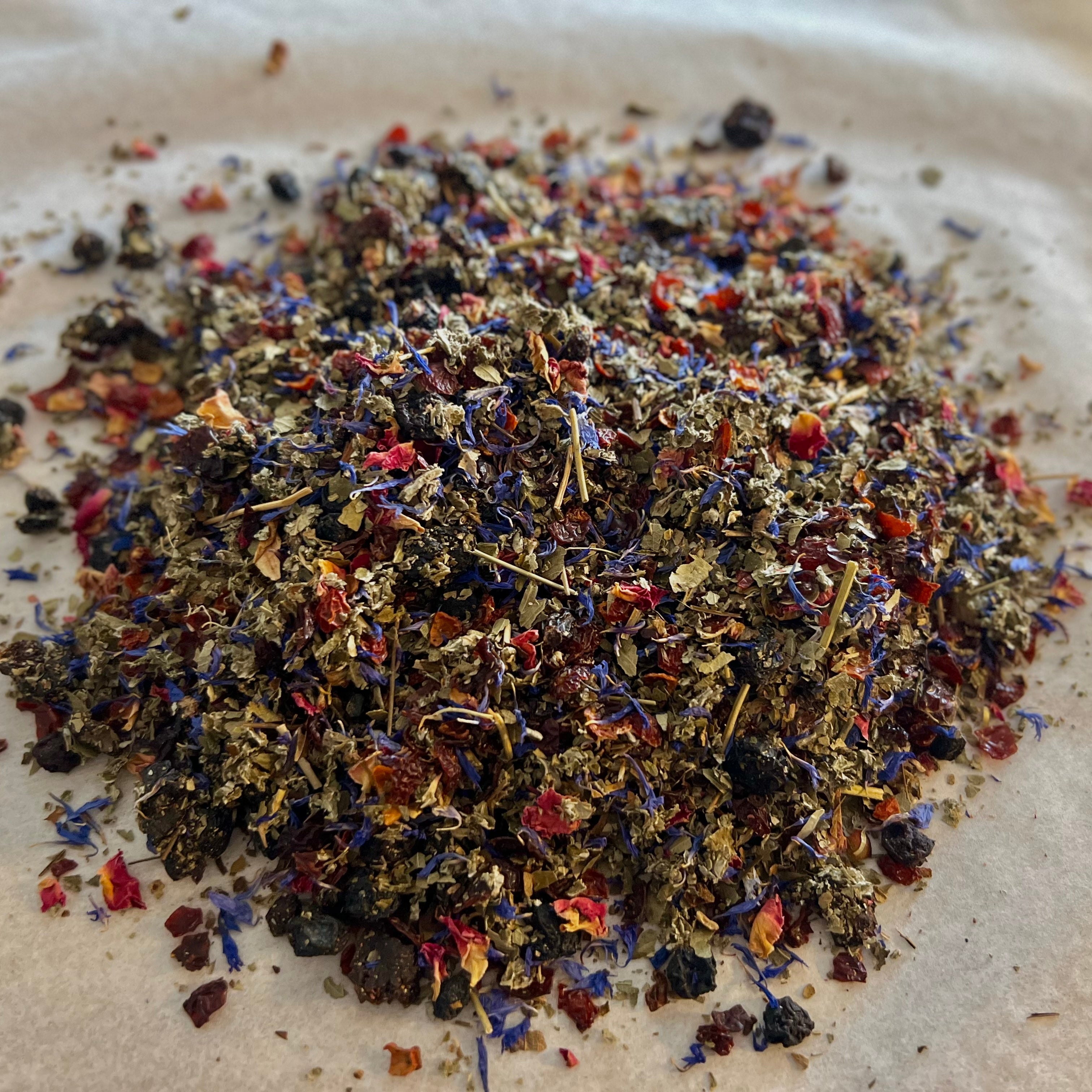 Close-up of Whispering Petals loose tea blend with rose petals, rose hips, cherry, blueberry, raspberry pieces on a light surface