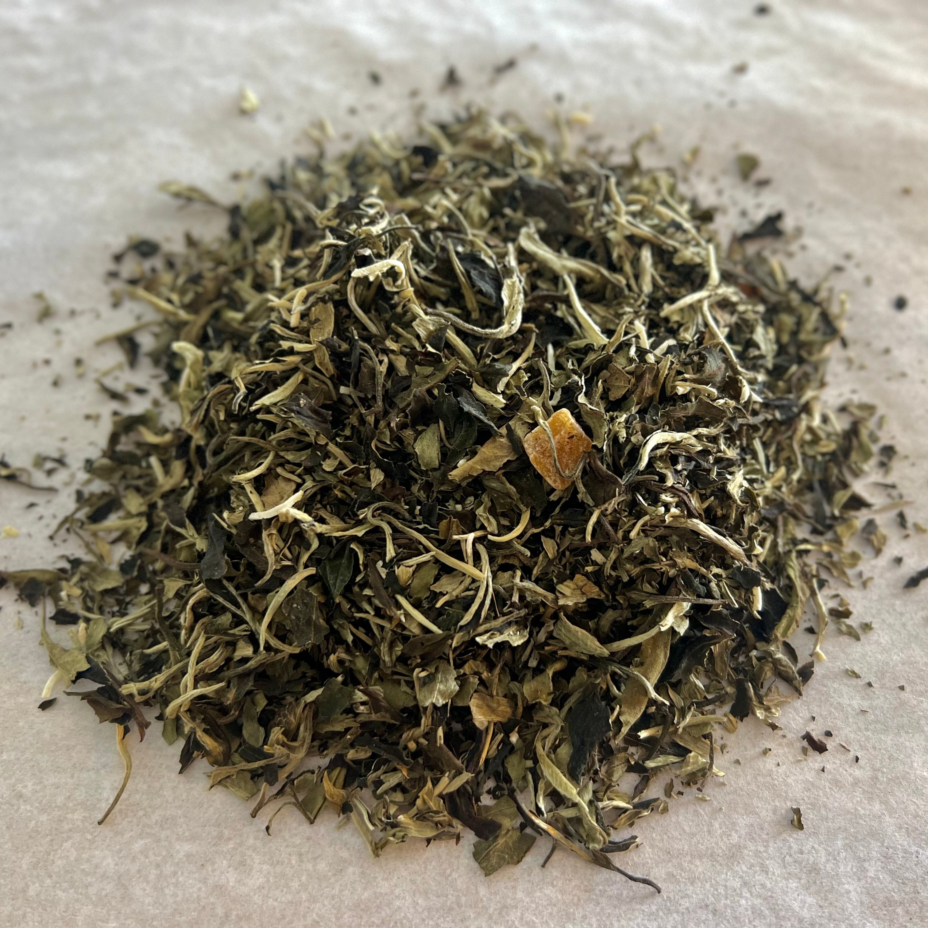 Close-up of loose White Tea blend with shredded coconut and pineapple pieces on a light parchment background